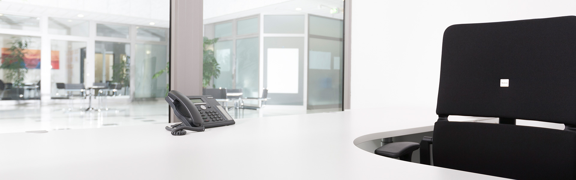 Helles Büro mit weißem Tisch und schwarzen Bürostuhl